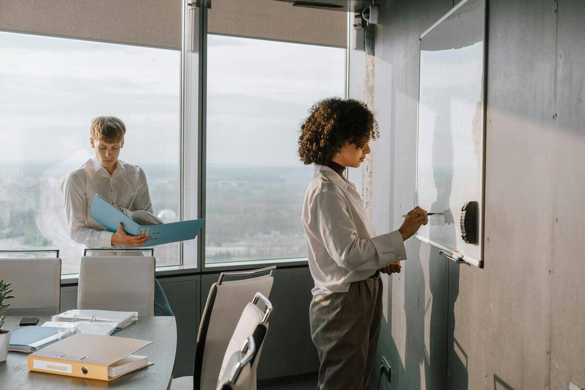 Dos profesionales colaborando frente a una pizarra en una oficina, trabajando en estrategias para impulsar su crecimiento laboral.